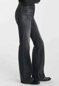 Jeans de mezclilla negros de tiro alto y corte acampanado con bolsillos frontales, un desvanecimiento sutil y corte recto, complementados con zapatos negros brillantes.