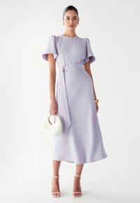 LilaMidi obleka z nabranimi rokavi, pasom z okroglo spono in gladkim materialom. Dopolnjena z belo torbico in sandali s trakovi.