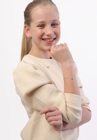 Zilveren hartvormige sieraden, waaronder een ketting en armband, gepresenteerd tegen een licht beige trui met een zachte textuur en subtiele glans.