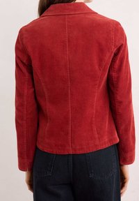 Giacca in velluto a coste rossa con colletto strutturato, righe verticali e maniche lunghe. Vestibilità sagomata con una leggera svasatura all'orlo.