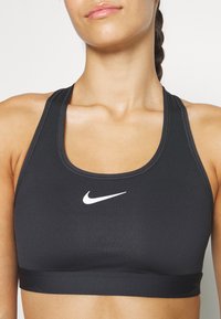 Black sports bra made of smooth fabric, featuring a round neckline and wide straps. It has a small white Nike logo on the front.