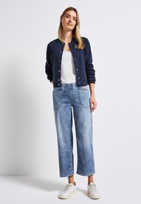 Veste de bombardier navy, débardeur blanc et pantalon large en bleu clair avec un lavage dégradé ; présente une taille élastique et des poches latérales.
