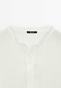 Chemise blanche à boutons avec un col rond et une étiquette noire visible indiquant « Massimo Dutti, Made in China ».