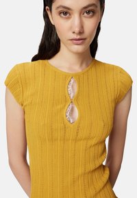 Top giallo senape con maniche corte a sbuffo, texture a coste e scollatura a chiave accentuata da dettagli in pizzo.