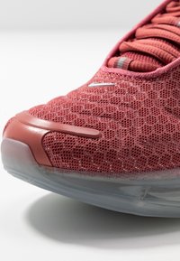 Röd sneakers i mesh med texturerad ovandel, plastdetaljer och en genomskinlig gummisula. Skosnören är matchade med skons färgschema.