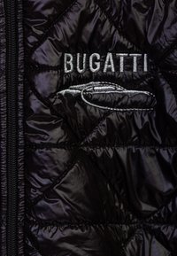 Giacca nera trapuntata con chiusura a zip, logo "Bugatti" ricamato e silhouette stilizzata di un'auto. Texture morbida e lucida con motivi diagonali.