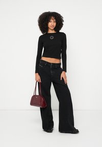 Čierny krátky dlhý rukáv s kruhovým logom, kombinovaný so širokými čiernymi džínsami a malou bordovou kabelkou. Obuv má lesklý povrch.