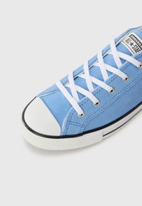 Baskets en daim bleu clair avec des lacets blancs et un capuchon en caoutchouc, présentant une bordure noire et une étiquette de logo sur la languette.