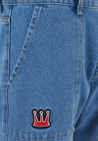 Helle blaue Denim-Shorts mit einem sichtbar roten und schwarzen gestickten Kronenlogo auf der rechten Tasche, ausgestattet mit klassischem Taschendesign und Nähten.