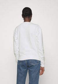 Valkoinen puuvillaneule, jossa on pyöreä kaula-aukko ja resorit, yhdistettynä sinisiin farkkuihin. Kangas näyttää pehmeältä ja teksturoidulta.