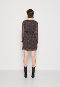 Vestido preto transparente com um padrão floral em rosa, vermelho e verde, com mangas longas, um cinto na cintura e punhos com babados. Botas pretas de tornozelo.