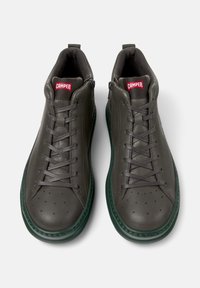 Ciemnoszare buty casualowe o eleganckim designie, z sznurowadłami i zieloną podeszwą, z logo "CAMPER" na czerwonych metkach.