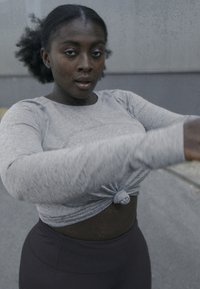 Gray long-sleeve top with a knotted front, paired with black high-waisted leggings. Smooth fabric with subtle texture, fitted design.