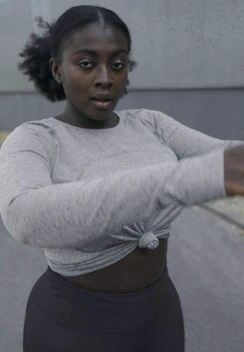 Grå langærmet top med knyttet front, parret med sorte højtaljede leggings. Glat stof med subtil tekstur, tætsiddende design.