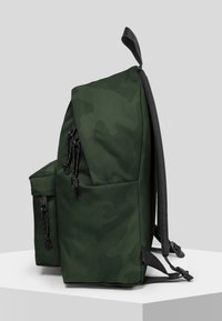 Mochila de camuflaje verde con un acabado de tela suave, dos bolsillos laterales, correas ajustables y una asa superior para un fácil transporte.