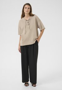 Beige vetershirt met brede korte mouwen, ontspannen pasvorm, gecombineerd met zwarte wijde broek en zwarte haksandalen. Zachte textuur van de stof.