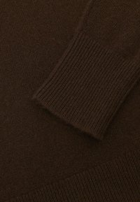 Tumepruun kootud kangas, millel on soonikuga detail varrukal, näidates kangasteksti ja õmblusmustreid.