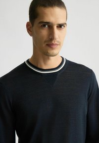Suéter azul marino con cuello redondo, que presenta un yugo texturizado y un cuello acanalado a rayas. Tejido suave con un acabado liso.