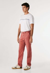 Pantaloni in denim rossi con una vestibilità comoda e una trama sbiadita, abbinati a una maglietta bianca con righe blu e un piccolo logo.
