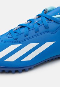 Sininen urheilukenkä, jossa on sileä synteettinen päällinen, valkoiset vinoviivat ja kuvioitu kumipohja pidon parantamiseksi.