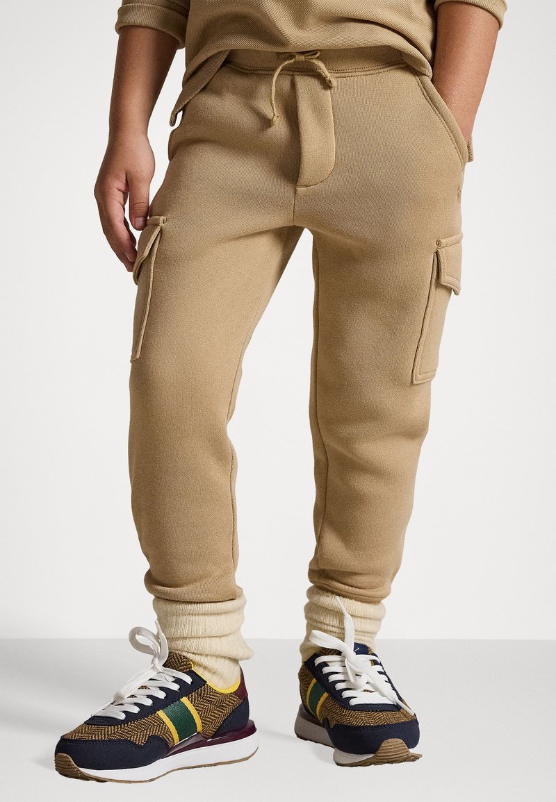 Sweatpants cargo bege com cintura elástica, bolsos frontais e punhos nas pernas, combinados com ténis retro multicoloridos.