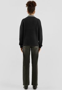 Czarny dziany sweter z teksturowanym wzorem, o luźnym kroju i ściągaczami przy rękawach, zestawiony z ciemnozielonymi jeansami o prostych nogawkach i czarnymi butami.