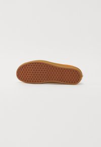 Semelle de chaussure présentée à plat avec une bande de roulement en caoutchouc marron présentant des motifs en losange et circulaires sur fond blanc uni.
