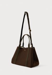 Καφέ τσάντα tote από ύφασμα με δύο κοντές λαβές και μία ρυθμιζόμενη μακριά ζώνη, χρυσό κούμπωμα και μικρό χρυσό έμβλημα μπροστά.