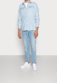 Jasnoniebieska koszula jeansowa z dwoma kieszeniami na piersi, zestawiona z jasnoniebieskimi obcisłymi jeansami i białymi trampkami. Gładka faktura, casualowy design.