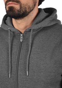 Grijze rits-hoodie met een trekkoordkap, met een gladde textuur, zilveren rits en subtiele stikdetails.