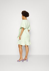 Vestido verde claro com padrão floral, mangas curtas e bufantes, cintura presa e bainha com volantes. Usado com sandálias de salto bloco cor lavanda.