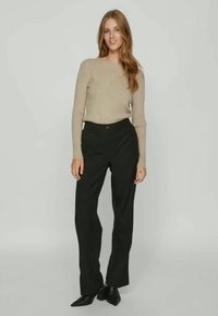 Beige ribbestrikket genser med lange ermer, kombinert med høyt liv svarte bukser. Buksene har rett ben-kutt og subtile frontfold. Svarte sko fullfører antrekket.