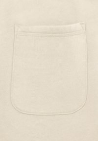 Beżowa tkanina z pojedynczą kwadratową kieszenią naszytą, posiadającą zaokrąglone dolne rogi i widoczne przeszycia na górze.