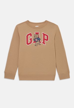 Sweat-shirt à manches longues de couleur tan avec les lettres rouges "GAP" et un ours dessin animé portant un pull marine avec un "G" rouge au centre.