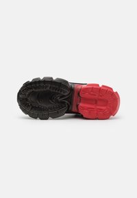 Semelle de chaussure avec des crampons profonds en caoutchouc noir et rouge, présentant des motifs de traction segmentés pour une adhérence et une durabilité accrues.