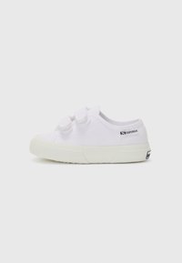 Zapatillas de lona blancas con punta redonda, dos correas de velcro y suela de goma texturizada; presenta una marca en el costado.