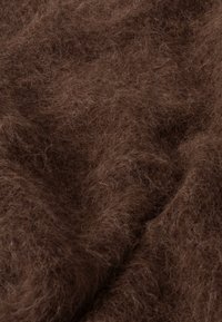 Tela marrón texturizada con fibras finas y suaves que crean una apariencia difusa, mostrando profundidad y variaciones en el color y el brillo.