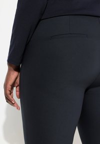 Marineblauwe legging gemaakt van rekbaar materiaal met een gladde textuur, voorzien van een klein achterzakje en een aansluitend ontwerp.