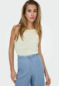 Top de tirantes de punto acanalado en amarillo claro con escote cuadrado, combinado con pantalones de mezclilla anchos de pierna recta en azul claro. Textura suave y ajuste casual.