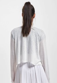 Weißes, leichtes, kurzes Oberteil mit langen Ärmeln und einem leicht durchscheinenden Material. Verfügt über einen abgerundeten Saum und eine lässige Passform.