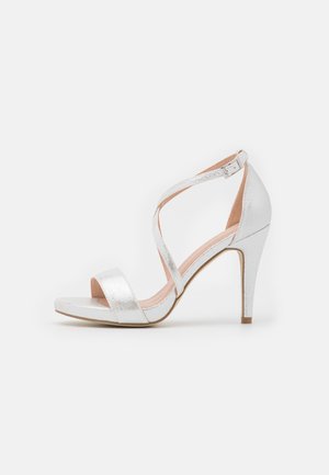 Srebrne sandały na obcasie z krzyżowanymi paskami, odkrytym noskiem i eleganckim, metalicznym wykończeniem oraz obcasem szpilką.