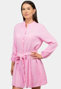 Abito button-up rosa con colletto, maniche lunghe, vita regolabile e tessuto texture. Presenta un delicato motivo a ondulazioni e bottoni bianchi.