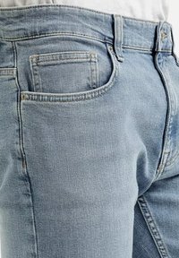 Jasnoniebieskie dżinsy z klasycznym pięcioma kieszeniami, subtelnym przeszyciem i lekko wyblakłą teksturą. Pas jest standardowy.
