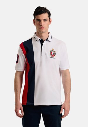 Camisa polo blanca con paneles a rayas en azul marino y rojo, cuello en contraste, logo bordado en el pecho y el número 3 en la manga. Fabricada en algodón.