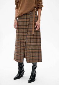 Bruine geruite midi rok met een wikkeldesign, met een zijsstrik, gemaakt van een gestructureerde stof. Gecombineerd met zwarte kniehoge haklaarzen.