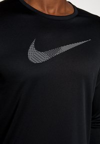 Nahaufnahme eines schwarzen Shirts mit einem großen, gemusterten, weißen Nike Swoosh-Logo auf der Brust, das von einer Person getragen wird.