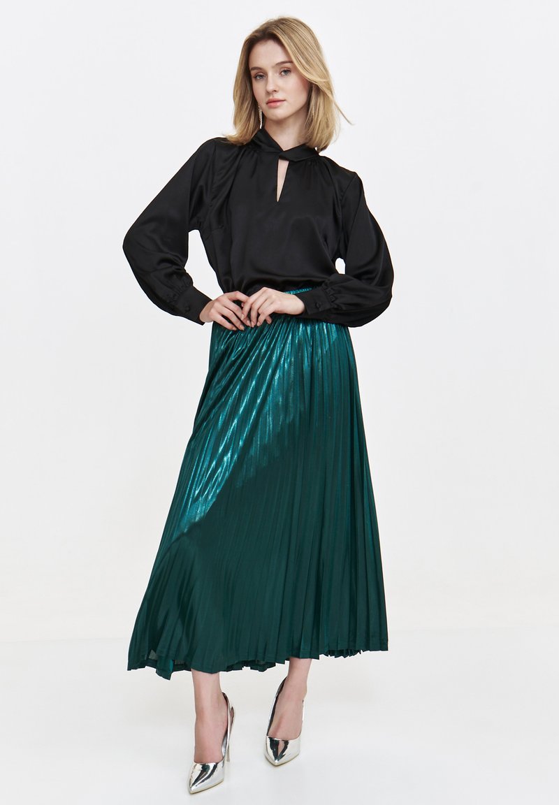 Black satin blouse with a keyhole neckline and long puff sleeves, paired with a pleated, shiny teal skirt and silver high heels.