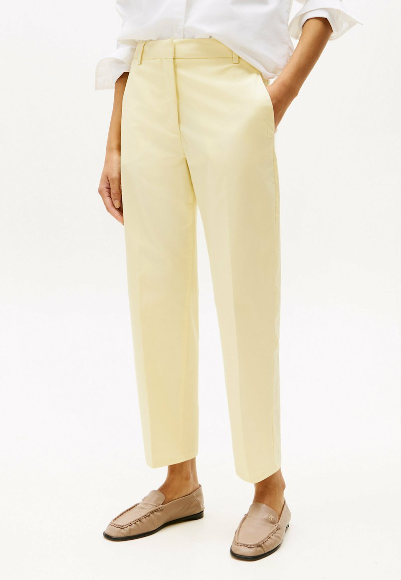 Slim-fit, lichtgele broek met een gladde textuur, op maat gemaakt ontwerp en rechte pijpen, gecombineerd met lichtbruine instappers.