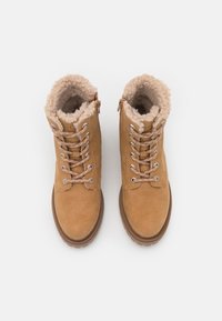Botas de tobillo de ante color tostado con forro de piel sintética, delantero con cordones y cremallera lateral. Suela de goma y ojetes metálicos para los cordones.