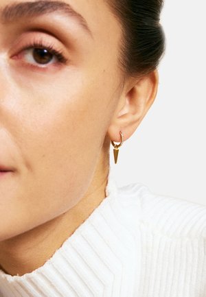 Gli orecchini a cerchio dorati presentano un design testurizzato con un accento a forma di cono appuntito. L'orecchio del modello è parzialmente visibile su uno sfondo neutro.